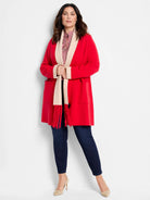 Red long cardigan with beige collar and cuffs, pockets, and a beige fringed scarf.
