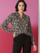 Black long-sleeve blouse with beige, brown, blue, and red spotted pattern. Collared neckline.