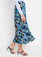 Pleated midi skirt in blues, greens, and beige abstract print on black background.