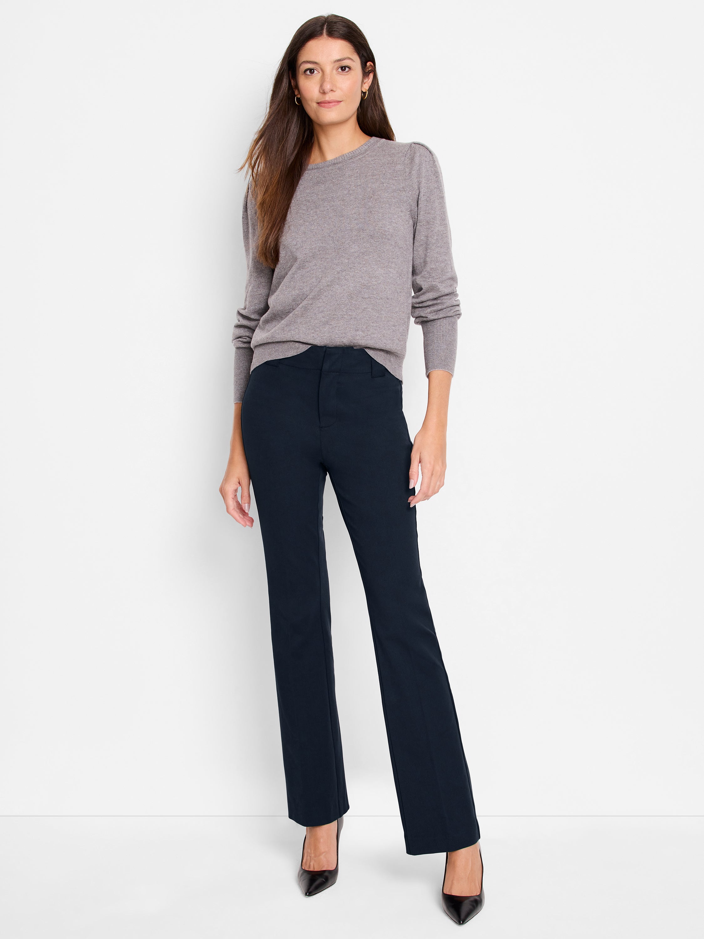 A model wears a taupe crewneck knit top paired with fitted navy high-rise trousers and black heels.