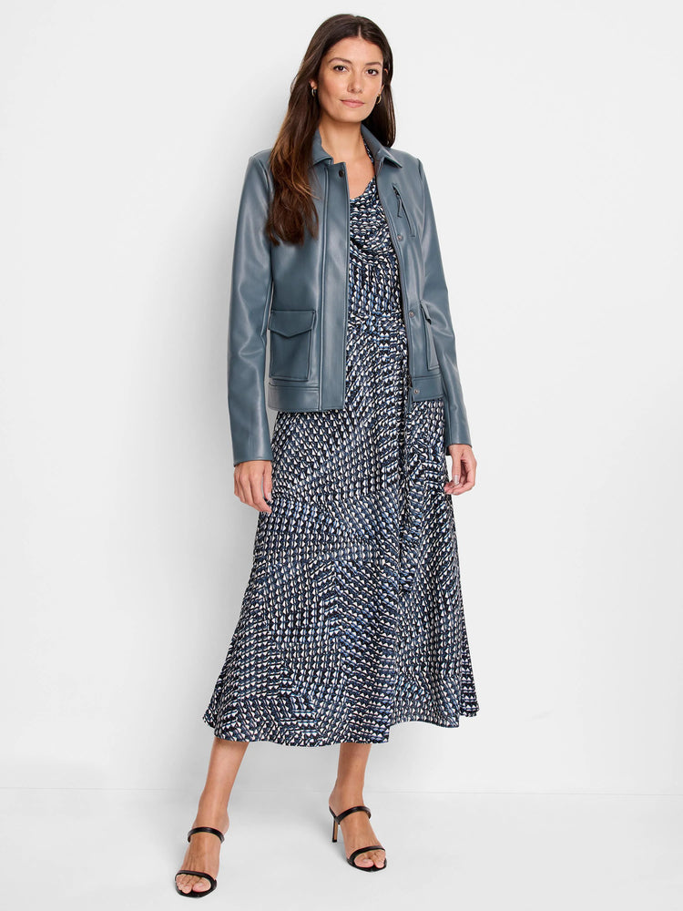 Teal jacket over a midi dress with a dark-blue, white, and light-blue geometric pattern.  The model wears black heels.