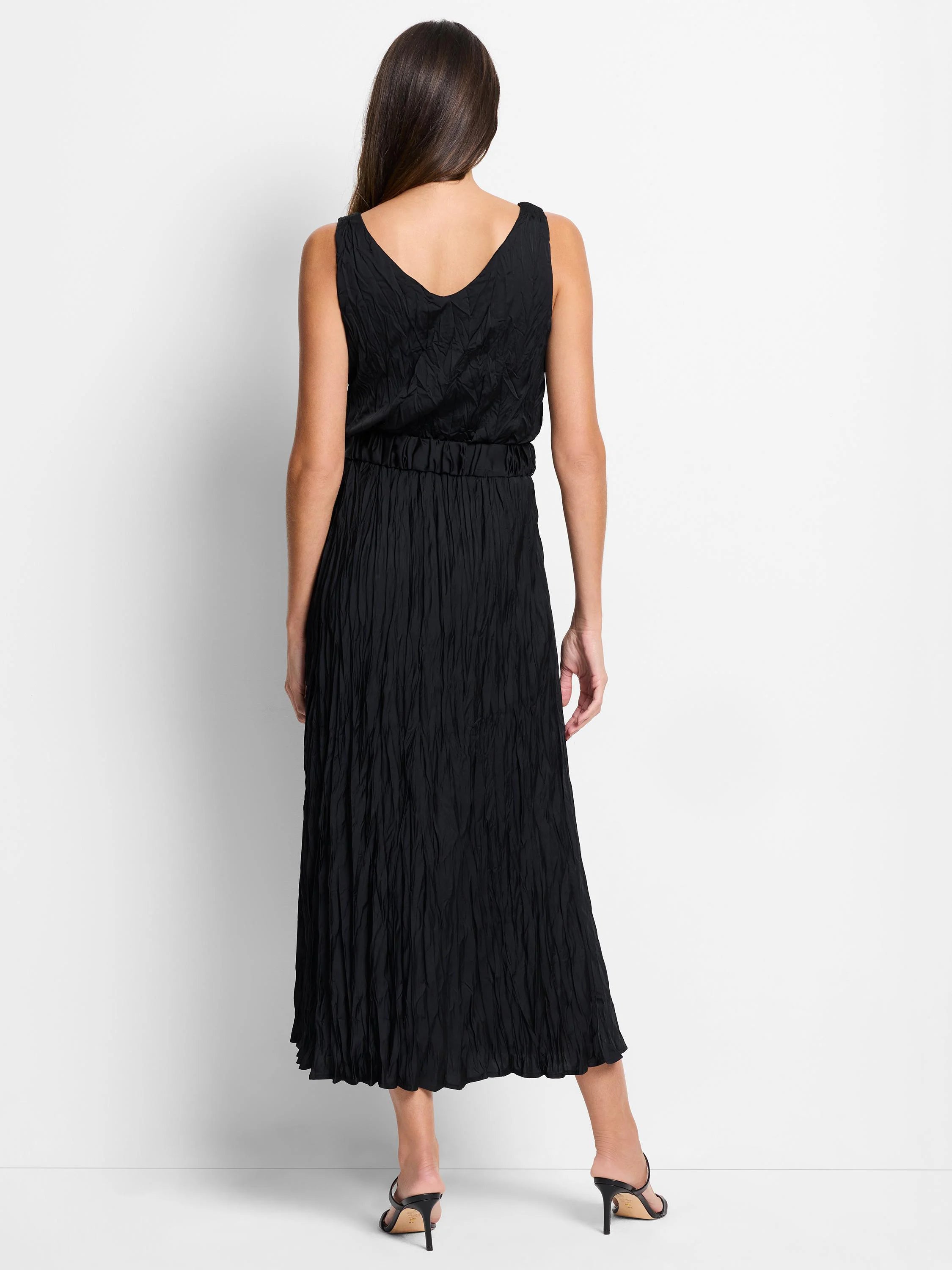 Black sleeveless midi dress.  Crinkled texture throughout. V-neck bodice and pleated skirt. Shown from the back.