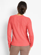 Back of a coral waffle-knit thermal top with a crew neck and long raglan sleeves. Model wears brown pants.