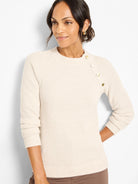 Off-white thermal waffle knit top with crew neck. Three gold buttons diagonally on left shoulder. Long sleeves.