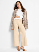 White, round-neck, long-sleeve knit top worn by a model, partially covered by a plaid jacket and beige pants.