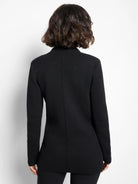 Black blazer, back view on model. Features long sleeves, a structured collar, subtle knit texture, and a central back seam.