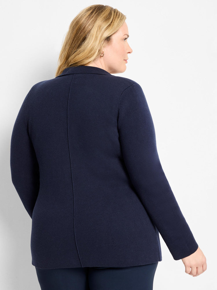 Navy knit blazer on a model, back view. Features fine ribbed texture, long sleeves, and a back seam.