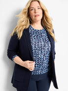 Navy knit blazer with lapels and front patch pockets, worn open over a patterned blue top.