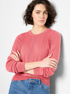 Coral pink crew neck sweater with fine knit texture, ribbed neckline, cuffs, and hem.