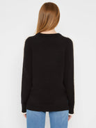 Black knit sweater with cream ruffles along sleeves and at cuffs. Back view.