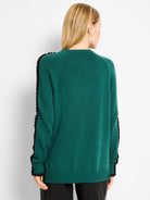 Dark green knit sweater with black ruffles on sleeves, black ribbed cuffs and hem, modeled from the back.
