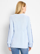 Light blue knit sweater, back view. Ruffles along sleeves are slightly darker blue. Ribbed cuffs and hem.