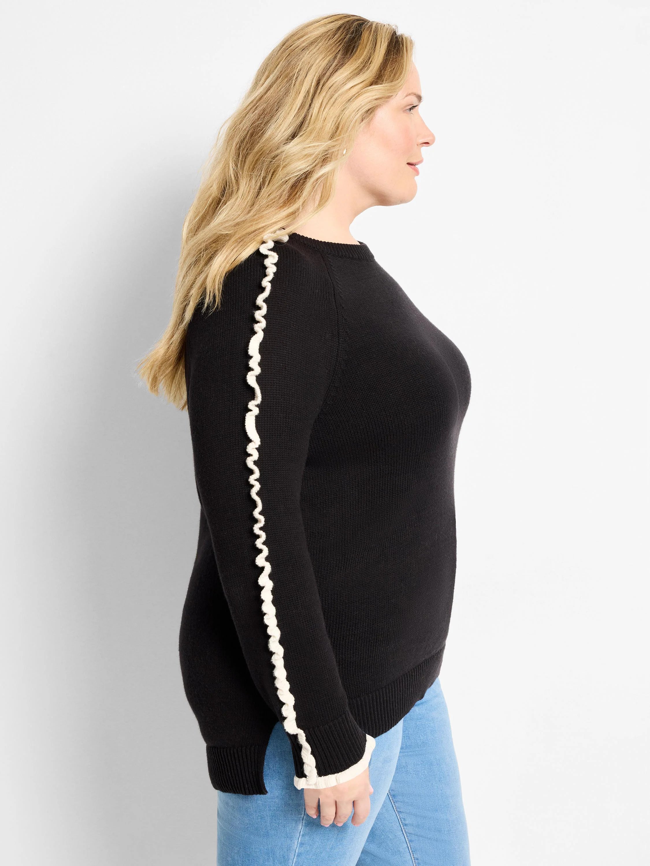 Black sweater with white ruffles along the sleeves and cuffs.