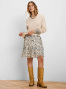 Light beige V-neck sweater, relaxed fit, ribbed cuffs & hem. Model wears it over a patterned dress.