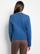 Back view of a blue knit bomber jacket with a ribbed collar and white zigzag stripes down the arms.