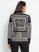 Black and white knit jacket with intricate geometric Nordic pattern covering the back and sleeves, worn from behind.