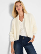 Cream fuzzy knit shrug cardigan with wide shawl collar and ribbed cuffs.