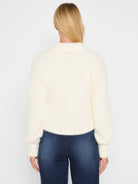 Cream fuzzy knit shrug cardigan. Cropped, with a collar and long sleeves. Back view on a model.