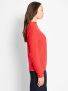 Coral-red pixel knit mock neck sweater with visible waffle texture and cuffed sleeves, paired with dark blue pants.