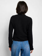 Black knit jacket, long sleeves, textured fabric, frayed hem and cuffs.  Rear view.