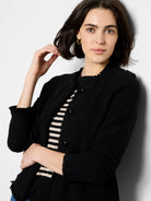 Black knit jacket with fringed edges, black buttons, and a textured weave.  A hint of a beige and black striped shirt is...