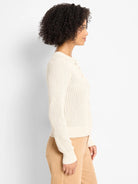 Cream open-knit button-front cardigan with perforated pattern and ribbed cuffs. Worn by a model from the side.
