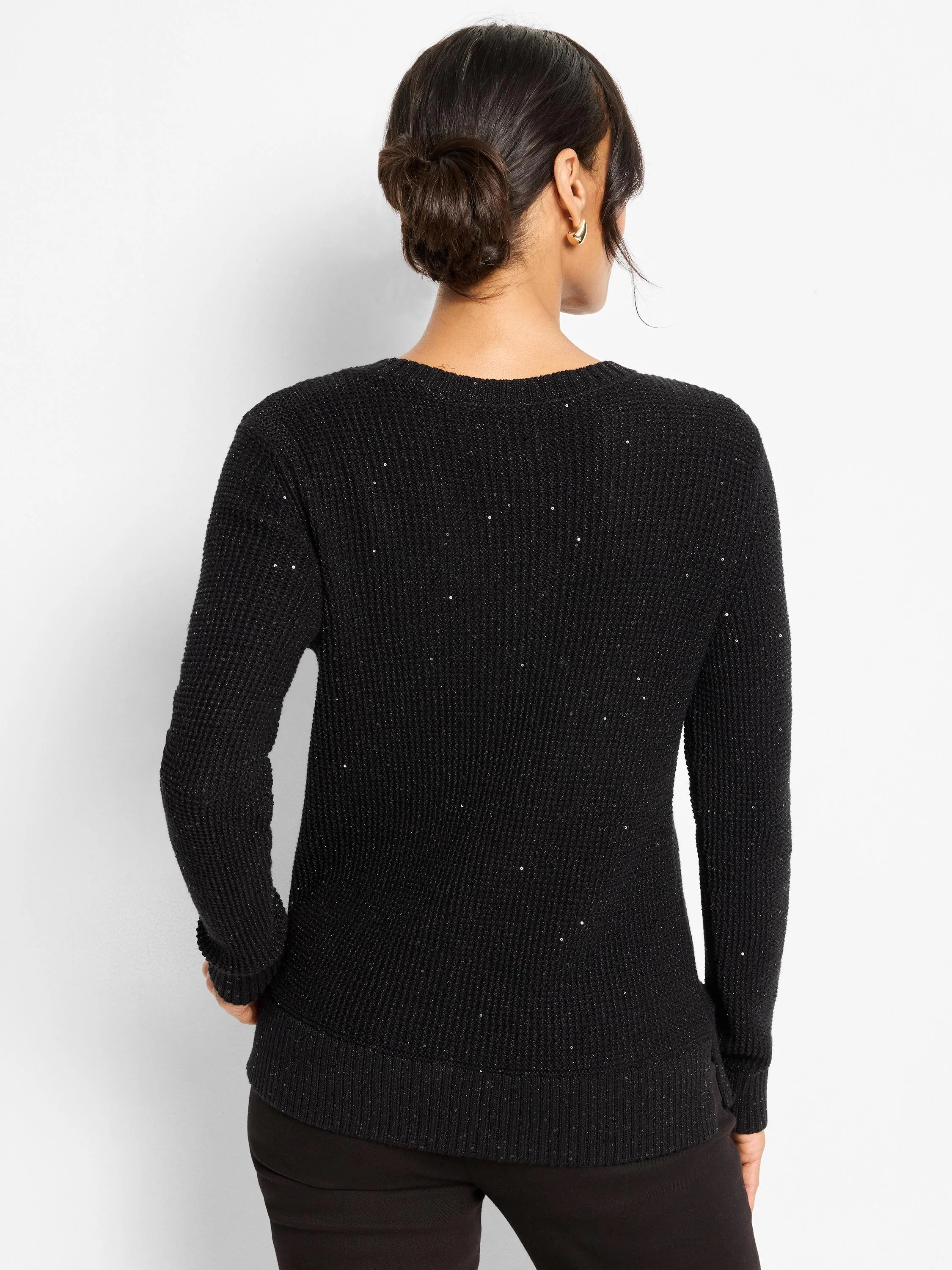 Black, long-sleeved waffle knit sweater with scattered silver shimmery specks and ribbed cuffs/hem. Model's back.