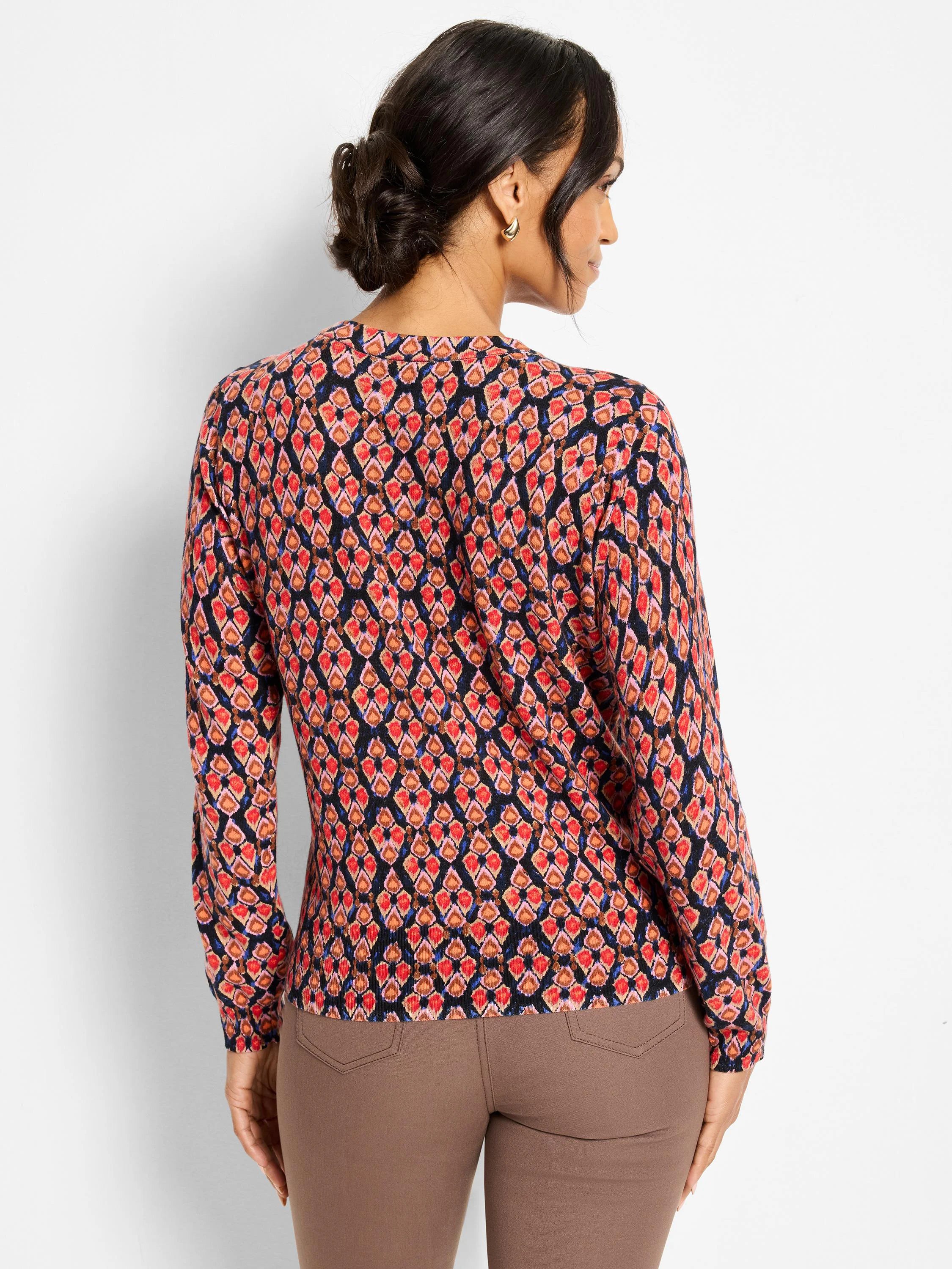 Long-sleeved sweater with red, orange, pink, and blue diamond ikat pattern on dark ground. Model's back.