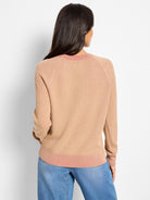 Tan textured sweater with coral pink ribbed collar, raglan seams, and hem. Model from back.