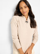 Beige knit sweater with mock neck, dark metal riding clasp, and ribbed cuffs.