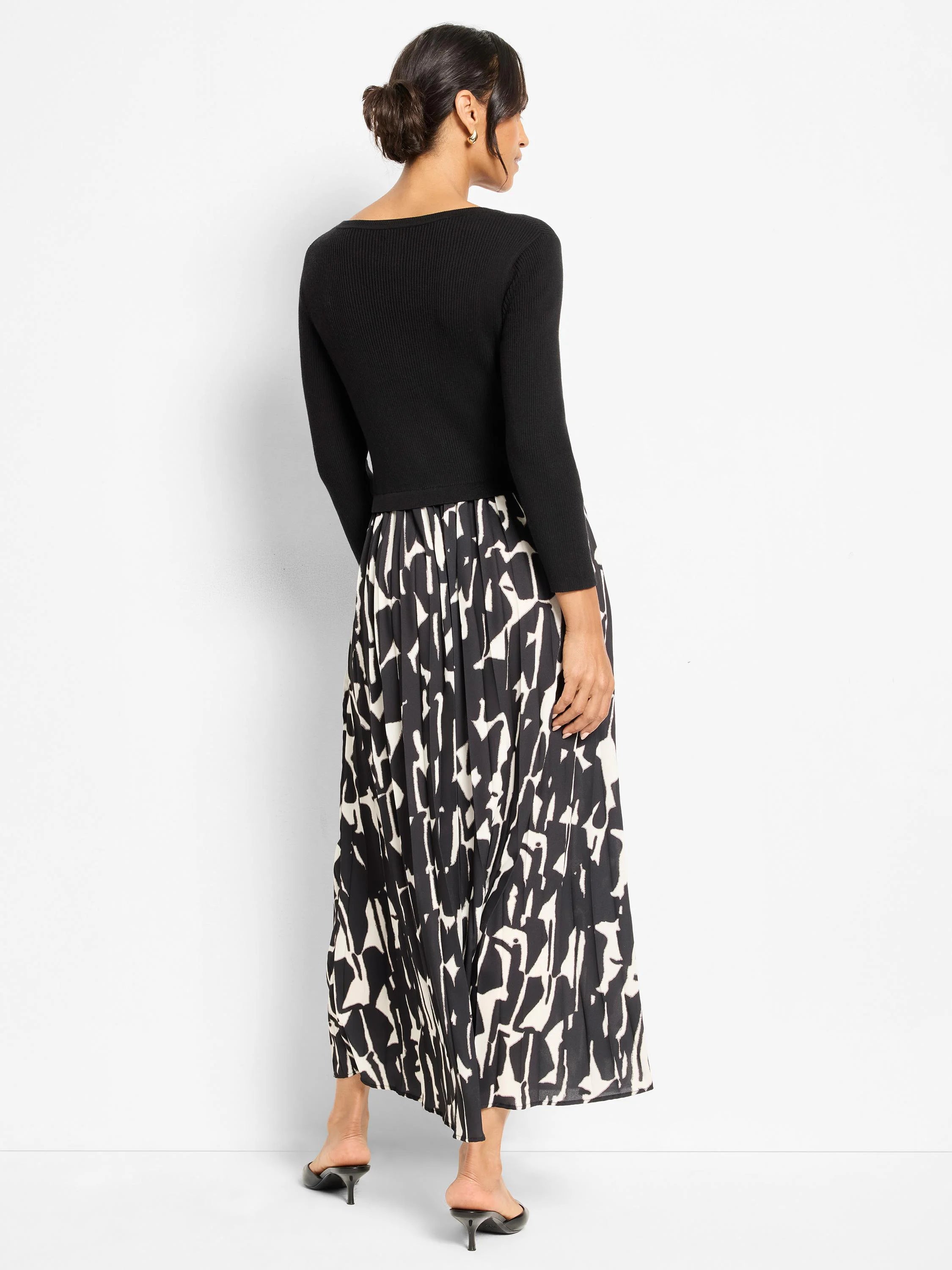 Black ribbed long-sleeve dress with a pleated maxi skirt in an abstract black and off-white print. Back view.
