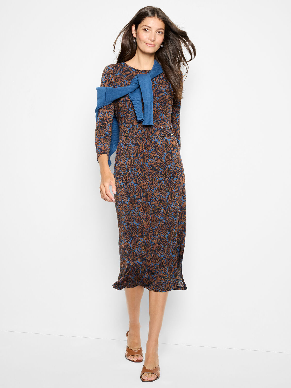 Woman wearing a patterned dress with a blue scarf against a white background