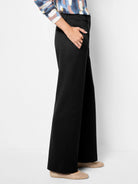 Black wide-leg trousers, full length. Hand in side pocket shows soft, drapey fabric.