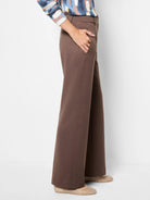 Brown drapey ponte wide-leg trousers on a model, with a hand in the pocket. Features a smooth fabric and full length.