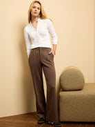 Brown wide-leg trousers feature subtle front pleats and a soft, flowing drape.