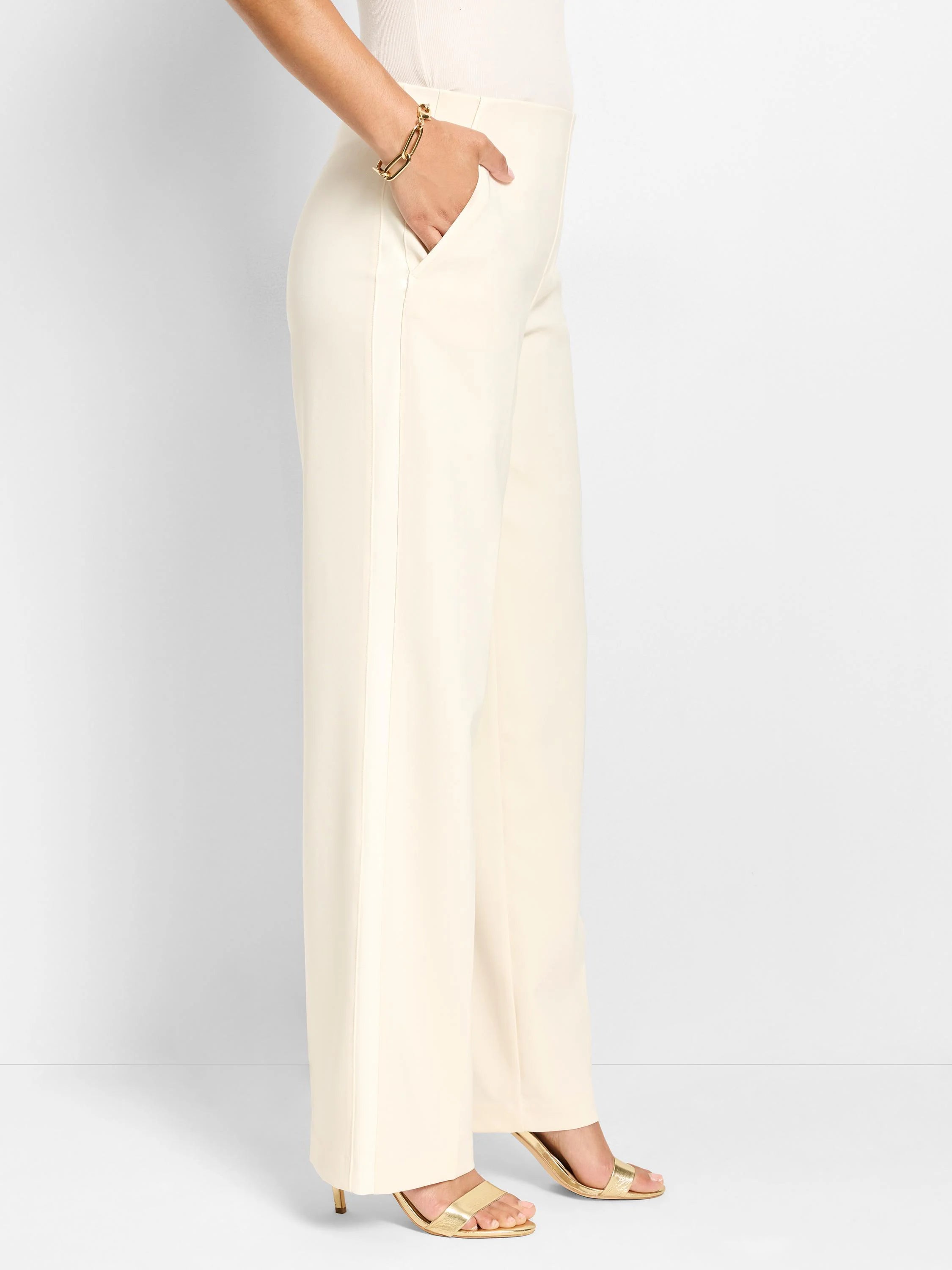 Cream wide-leg pants with front vertical crease. One hand rests in a side slash pocket.