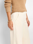 Cream wide-leg tuxedo pants with sleek fabric, vertical front seams, and an angled hip pocket.