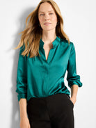 Glossy emerald green shirt with a V-neck and long sleeves, worn by a woman.