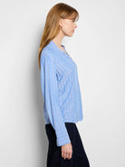 Light blue, vertically striped shirt with white stripes and ruffled neckline. Long sleeves.