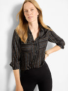 Black button-up shirt with vertical white, tan, and brown painted stripes. Features collar, chest pockets, and rolled...