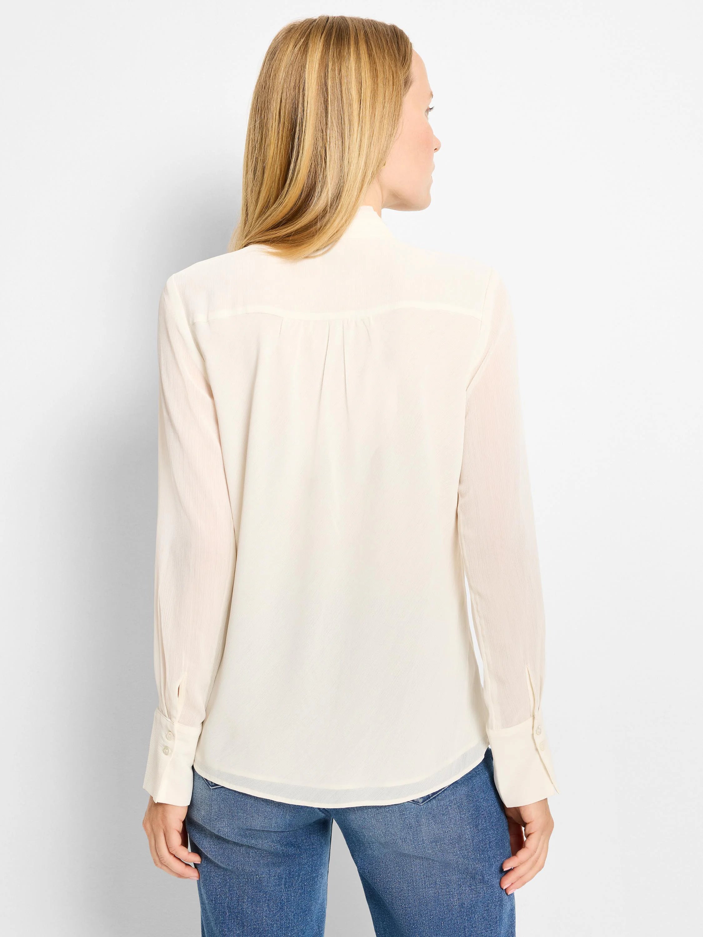 Cream sheer chiffon top, back view. Features pleated back yoke, long sleeves with buttoned cuffs, and a curved hem.