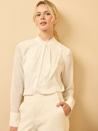 Off-white chiffon top with long sheer sleeves, ruffled mock neck, and flowing vertical pleats down the front.