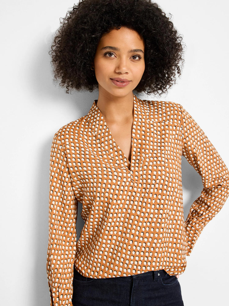 Rust-colored long-sleeve top with off-white, dark-outlined dots and a split V-neck.