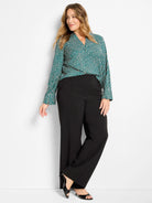 Deep teal long-sleeve V-neck top with an all-over pattern of irregular cream-colored dots.