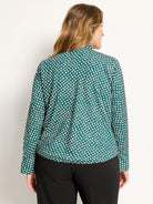 Model's back view of a teal long-sleeve top with off-white dots, outlined in dark, and a band collar.