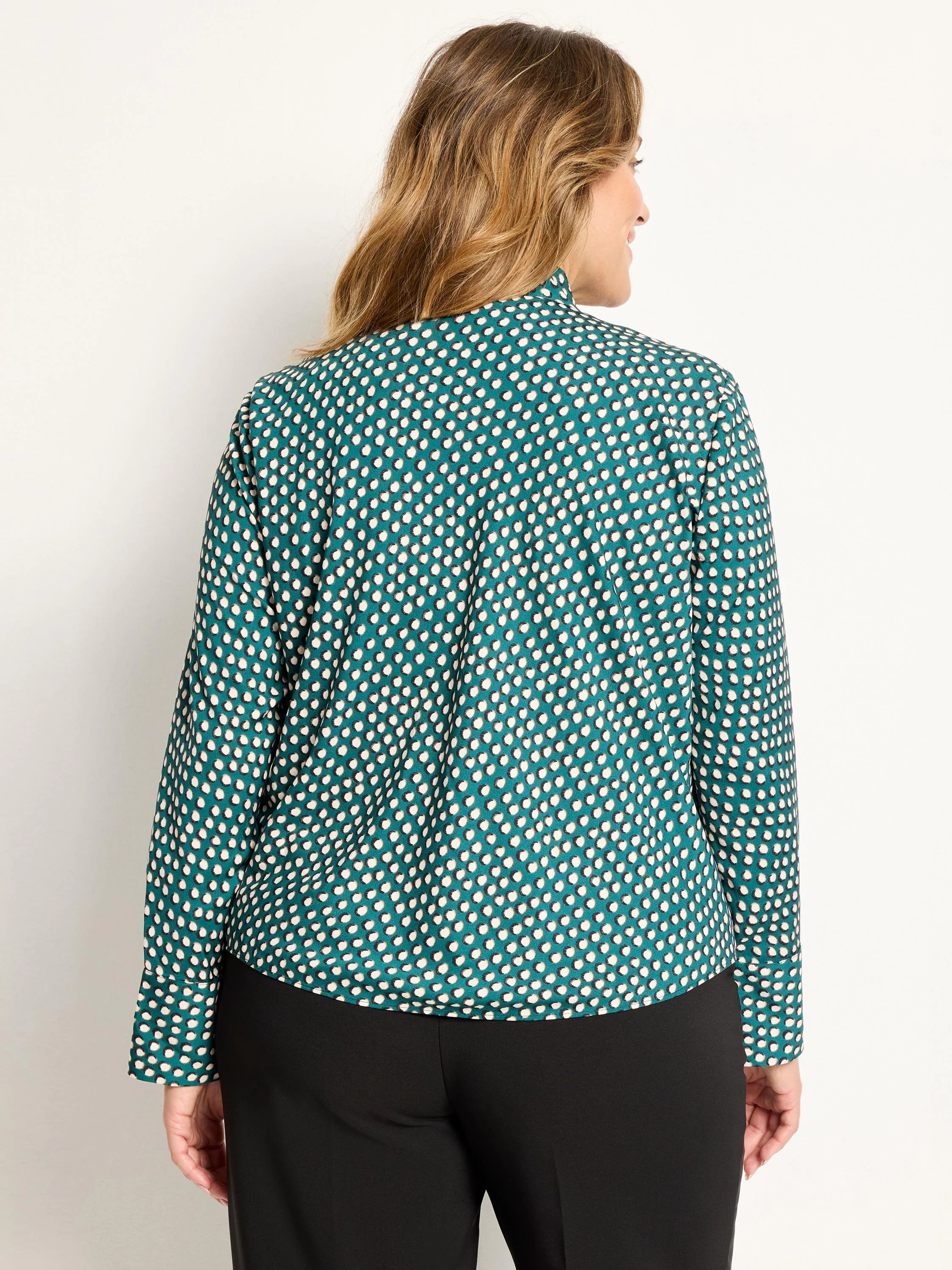 Model's back view of a teal long-sleeve top with off-white dots, outlined in dark, and a band collar.