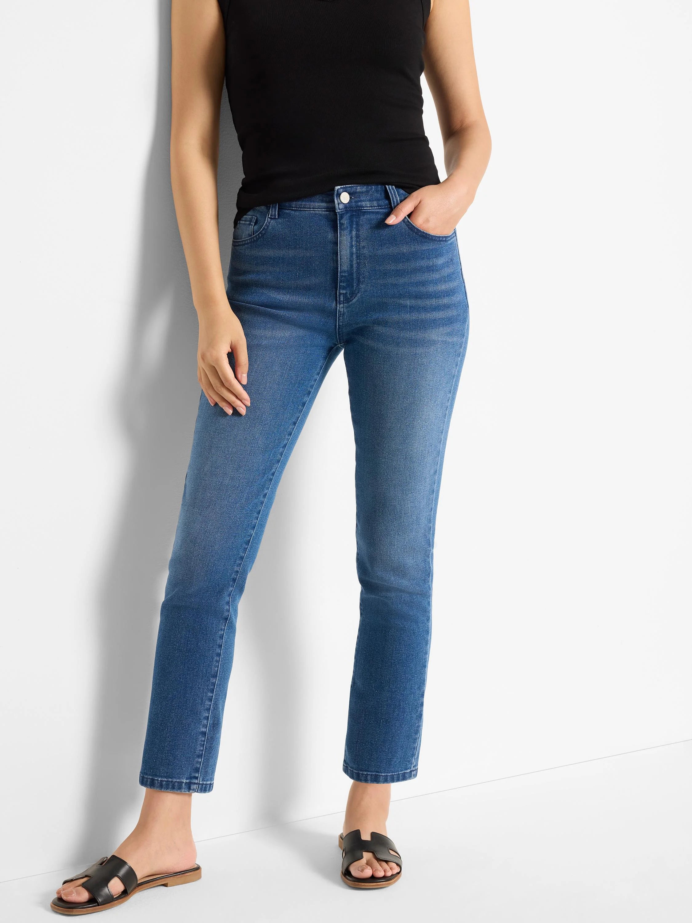 Mid-blue straight ankle jeans with subtle thigh fading, worn by a person.