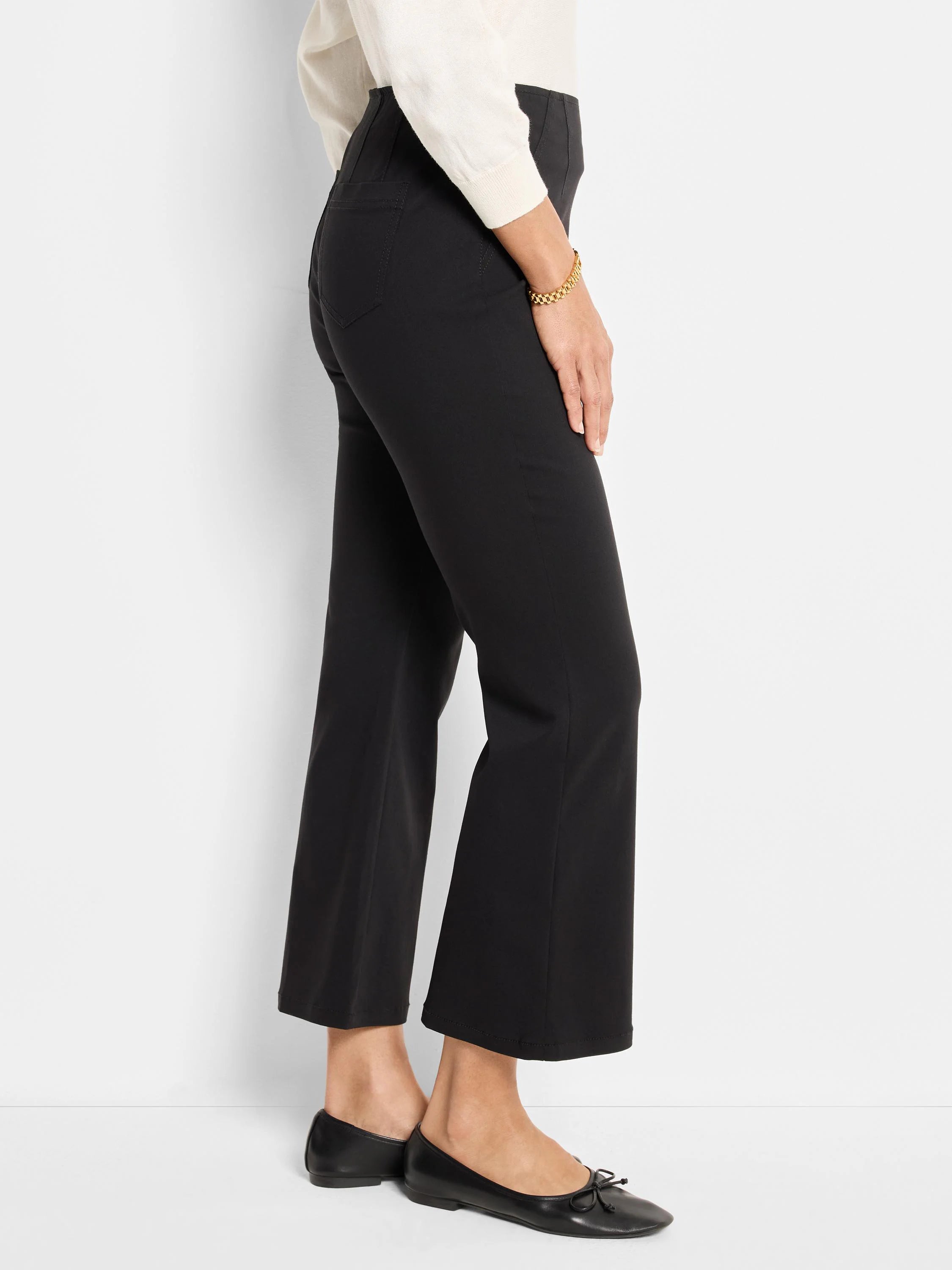 Black, high-waisted bootcut pants with a cropped leg, worn by a person from the side.