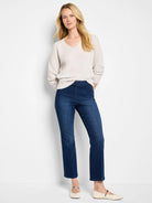 Dark wash blue boot-cut jeans on a model.  The jeans are shown with a light beige sweater and light beige flats.