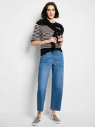 Model wears medium blue, high-waisted barrel leg jeans, cropped above the ankle.